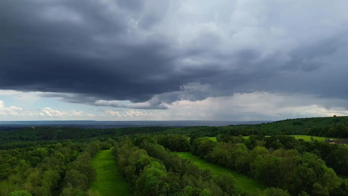 Aerial view of a forested landscape with dark storm clouds gathering overhead.